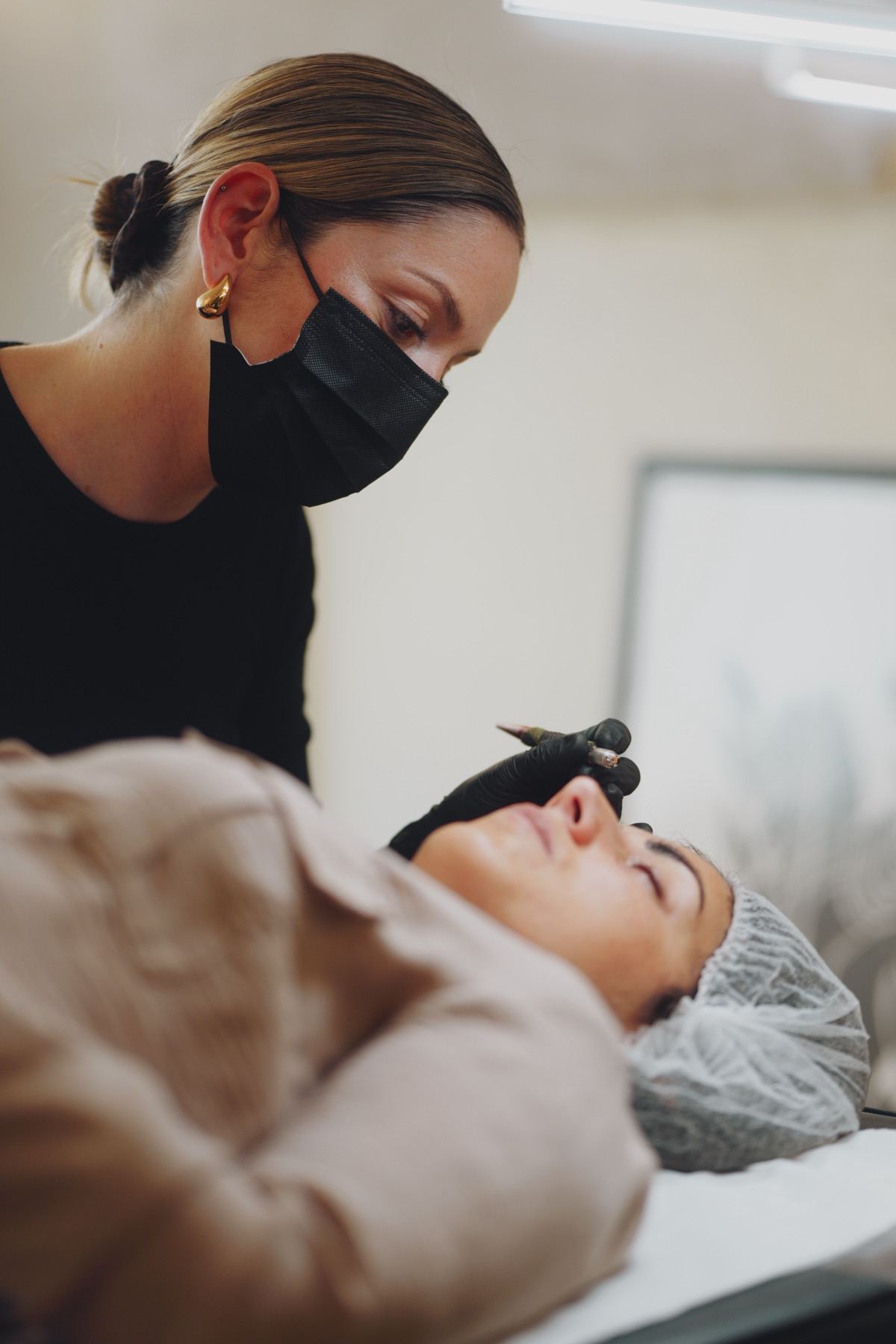 Claire Degli-Esposti penchée sur une cliente allongée, stylet en main, pendant une séance de maquillage permanent à Aix-les-Bains