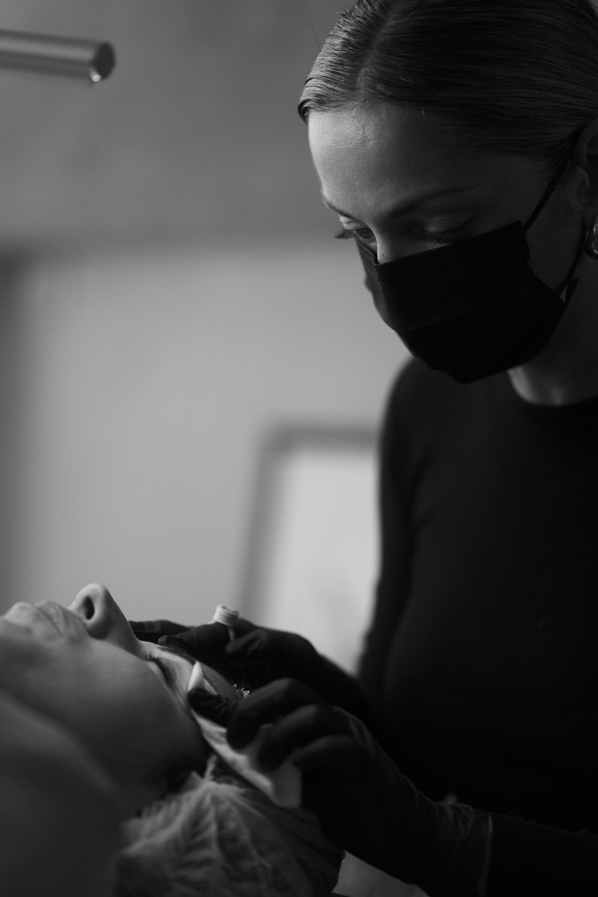Claire Degli-Esposti au travail en noir et blanc, penchée sur une cliente allongée, dans son espace d'Aix-les-Bains